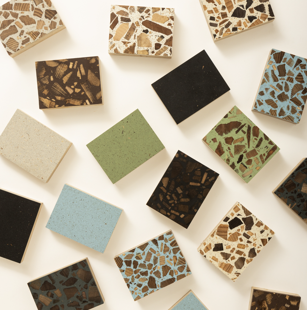 Multiple rectangular wooden samples lay flat across a white background. The wood samples each have a different terrazzo speckled colour finish including brown's, greens, blues and stone.