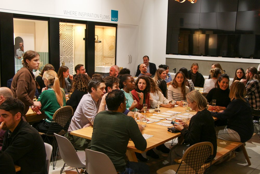 image of lots of people sat around the table playing bingo, with drinks and snacks. TV screen in the background.