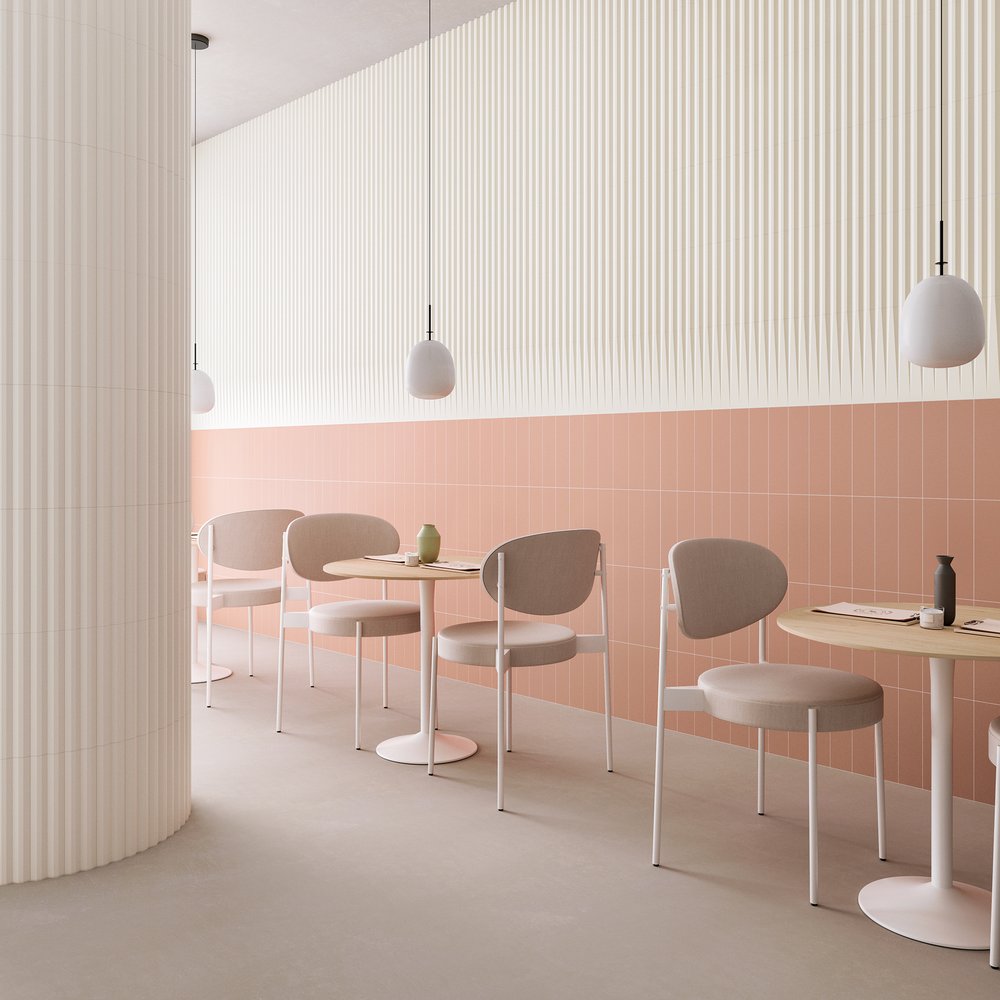 Image of cafe with restaurant chairs two to each small tale. The walls are white tiles to the top, and cotto peach coloured to the bottom half of the wall. Single pendant lights hang from the ceiling.